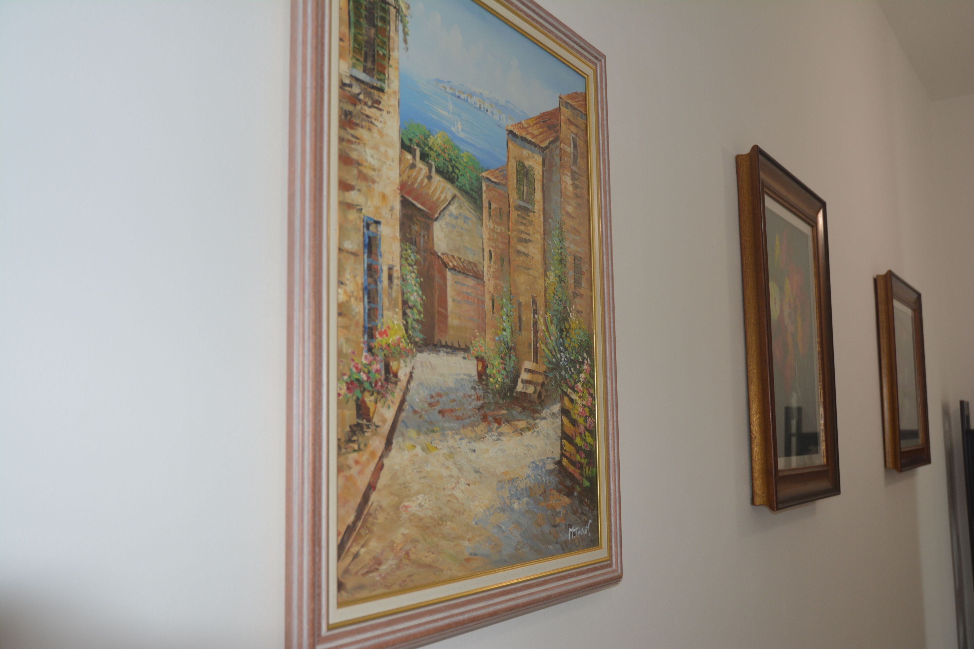 A hallway with a large framed painting of a street scene, two smaller framed pictures, and a radiator on the wall.