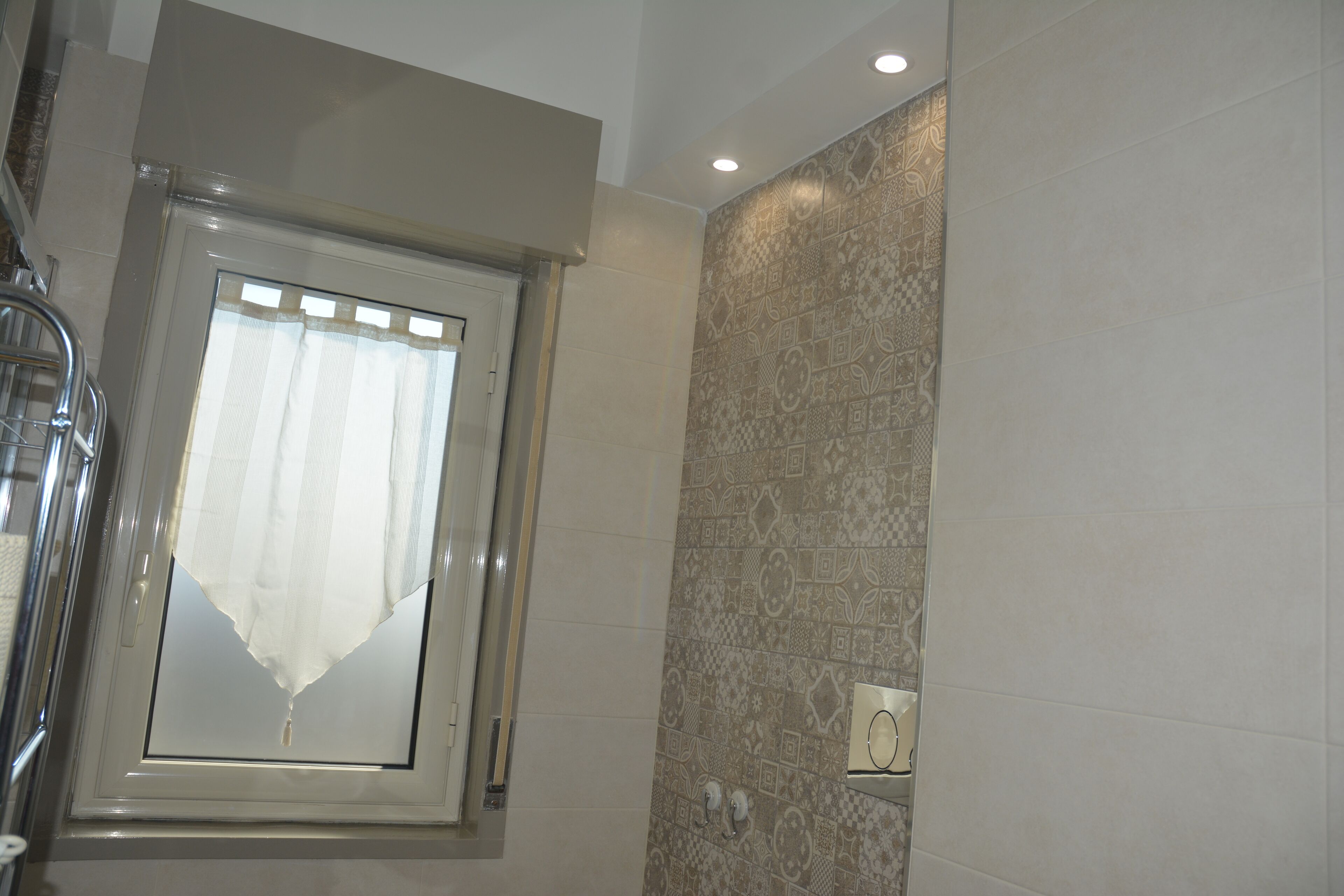 Une salle de bain avec une fenêtre, des carreaux décorés et un porte-serviettes.