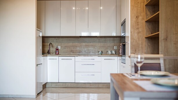 A modern kitchen with white cabinets, a wooden countertop, and a dining area with a table and chairs. - Modern Apartment (Warsaw)