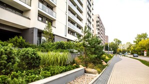 A modern building with multiple floors, a paved walkway, and landscaped areas with various plants. - Silver Apartments - ul. Klopot (Warsaw)