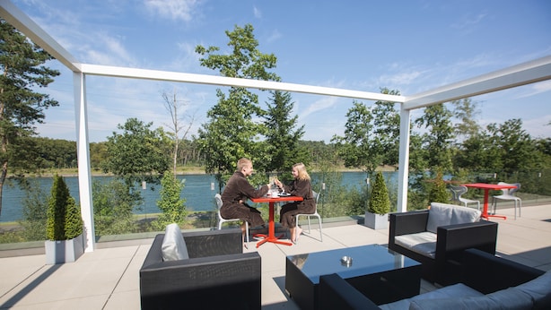 Un espace extérieur abrité, avec deux tables et des chaises, donnant sur un lac.