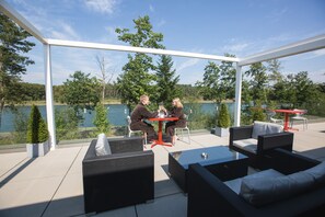 Een overdekt terras buiten met twee tafels en stoelen, met uitzicht op een meer.