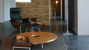 Un hall d’hôtel moderne avec un mur d’accent en bois, une table ronde en bois et des fauteuils en cuir noir.