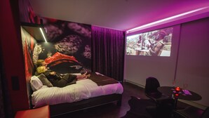 Une chambre d’hôtel avec un lit, une petite table avec deux verres et un écran diffusant un film.