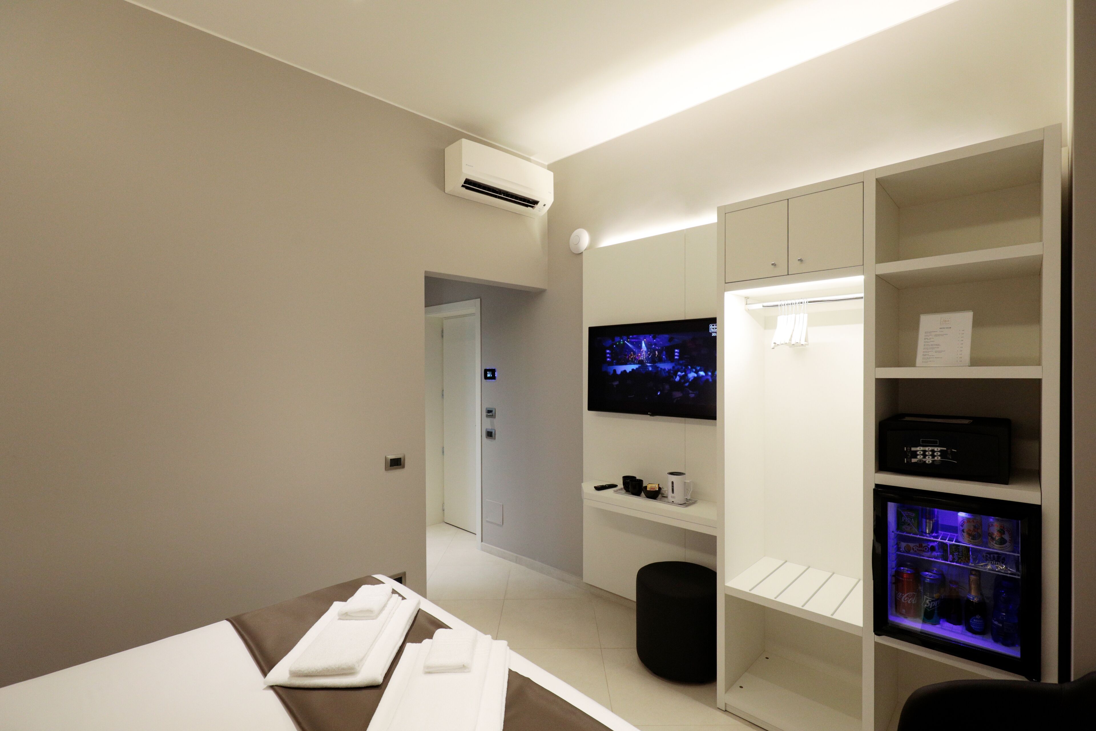 Una habitación de hotel moderna con televisión de pantalla plana en la pared, minibar y refrigerador pequeño.