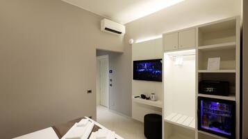 Una habitación de hotel moderna con televisión de pantalla plana en la pared, minibar y refrigerador pequeño.