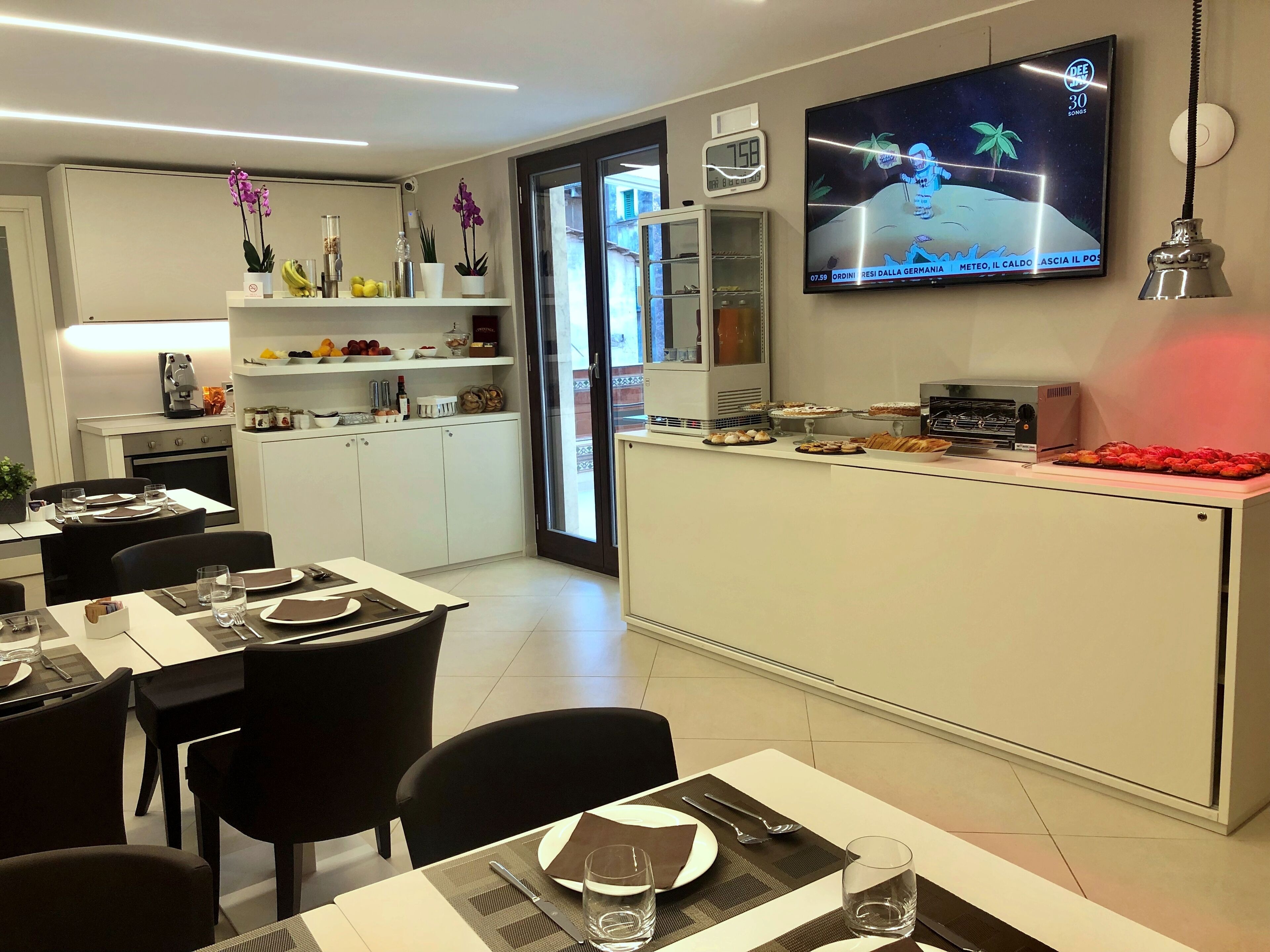 Una cucina moderna con zona pranzo, una TV che mostra un cartone animato e una macchina per il caffè.