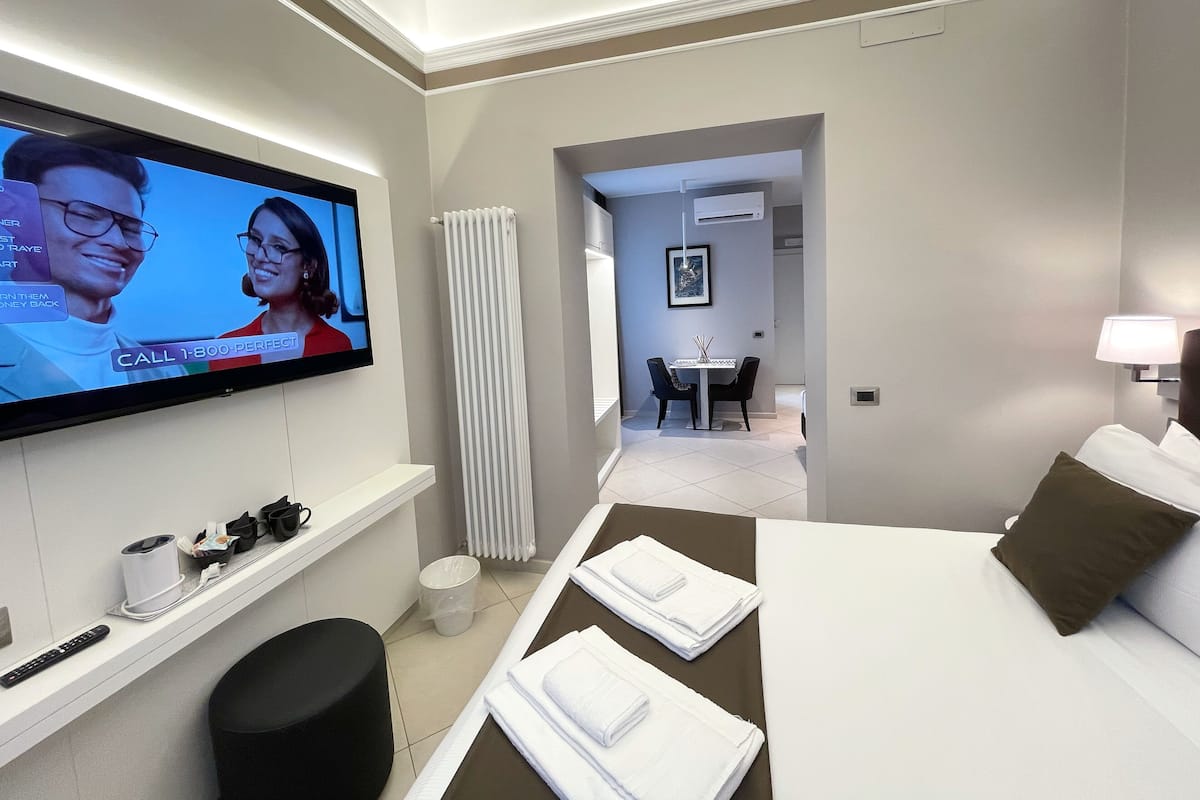 Una habitación de hotel con cama, televisor montado en la pared, una mesita con sillas y un radiador.
