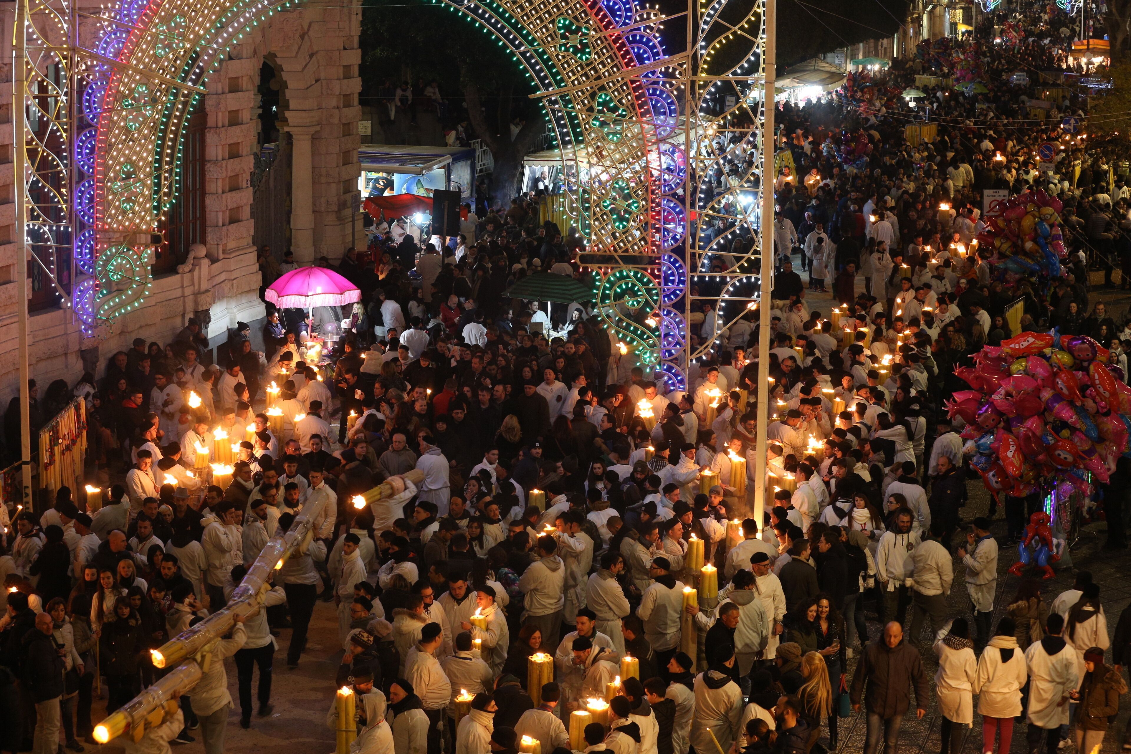 A crowded public square with people holding candles and a large arch decorated with lights.