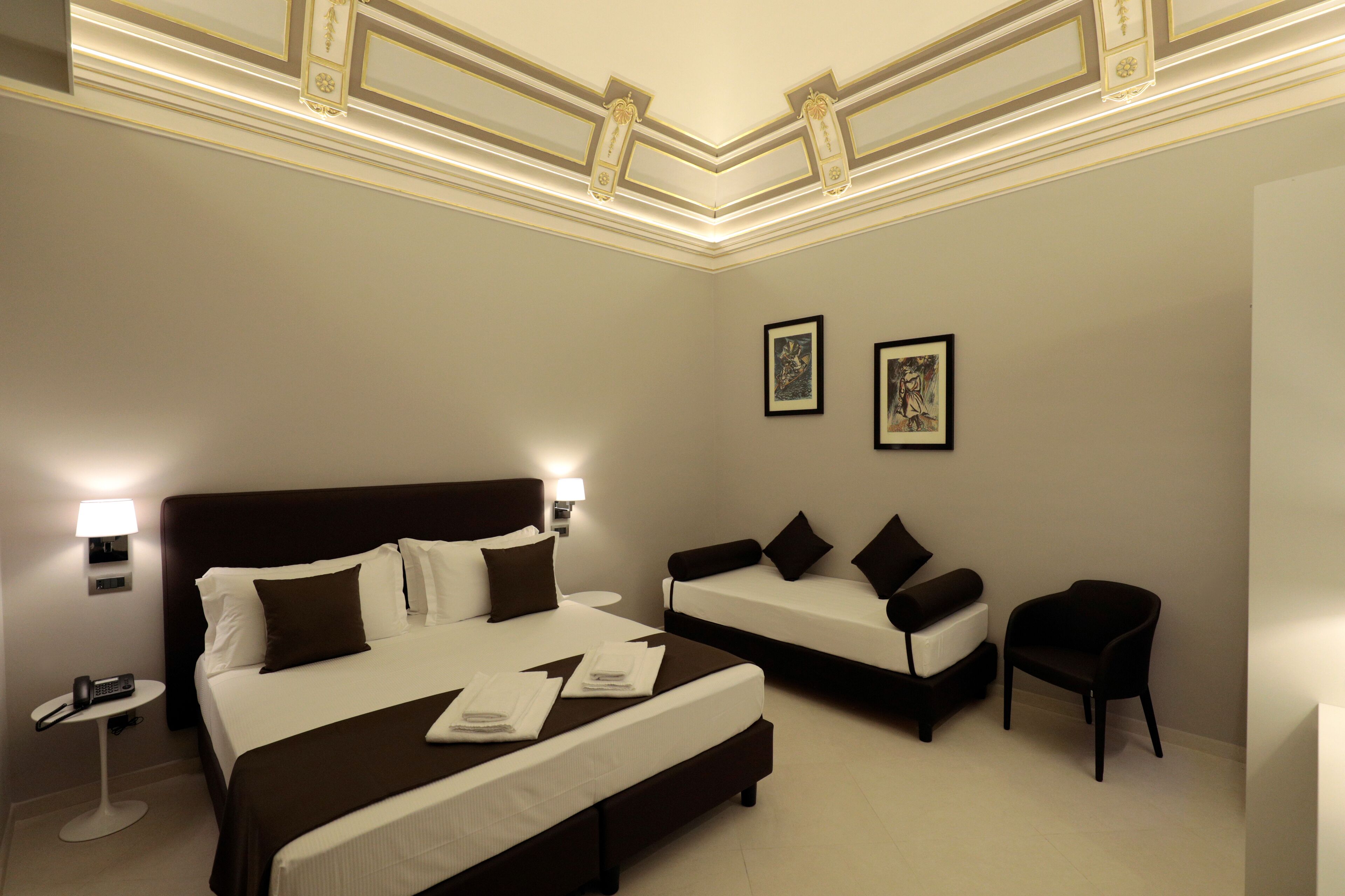A hotel room with a large bed, a smaller bed, a chair, and two framed pictures on the wall.