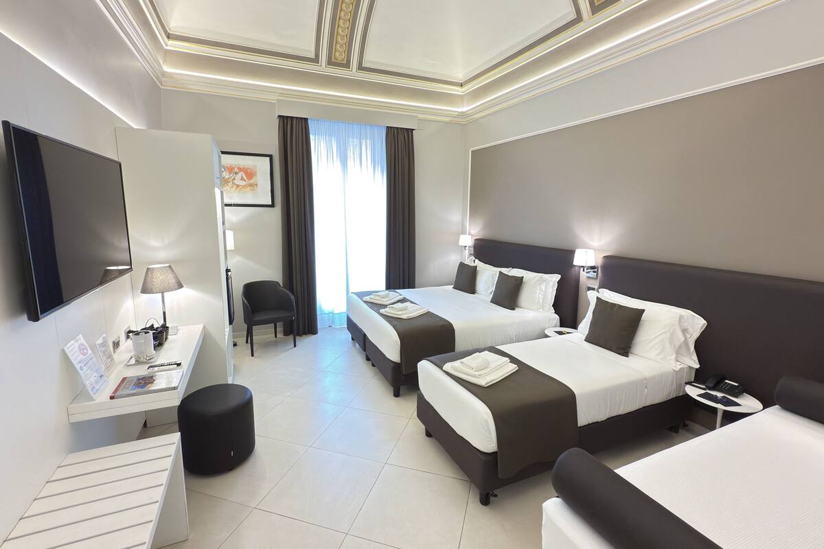 Habitación de hotel con dos camas, un escritorio, una silla, un televisor y una ventana con cortinas.