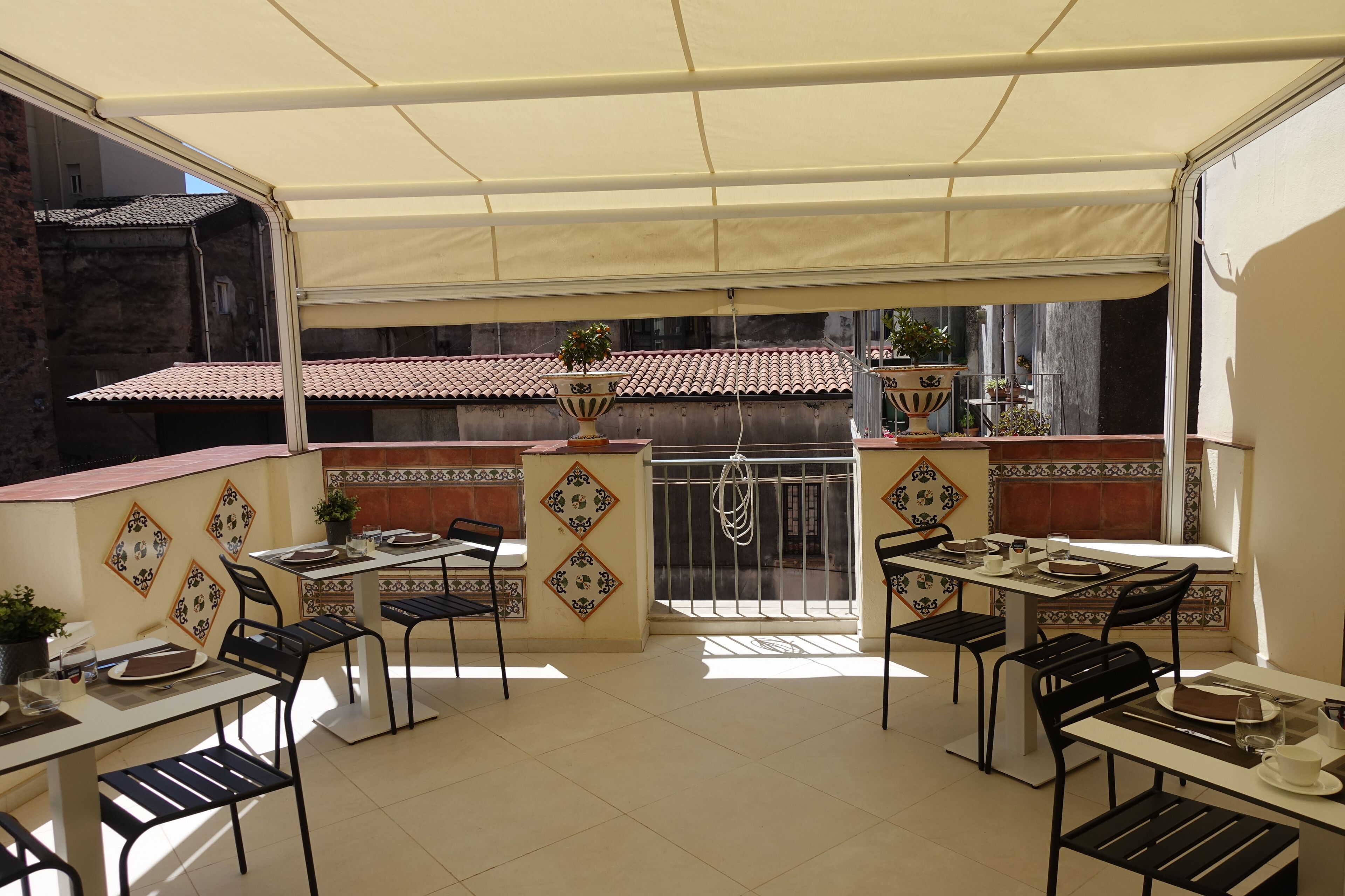 Un patio exterior con mesas y sillas, una zona cubierta y azulejos decorativos.