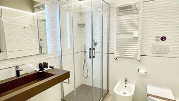 A modern bathroom with a glass-enclosed shower, a vanity with a sink, a bidet, and a toilet.