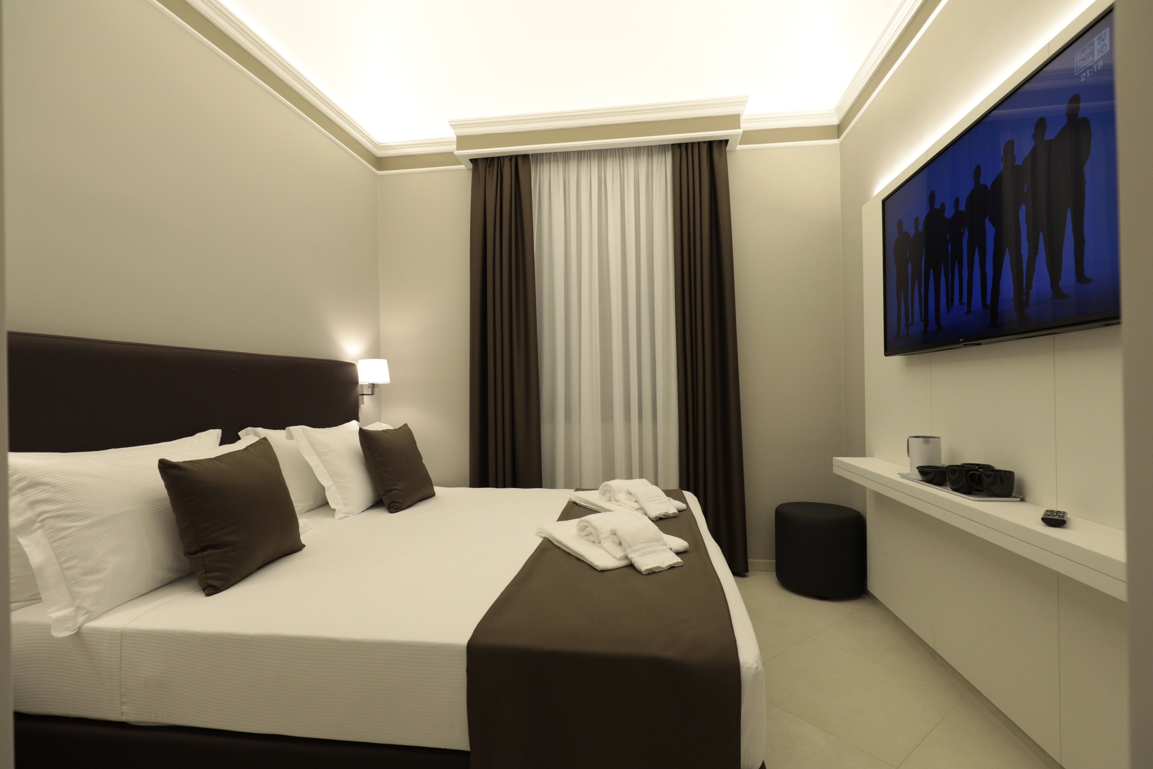 Una habitación de hotel moderna con una cama grande, un televisor de pantalla plana en la pared y un pequeño escritorio con una lámpara.