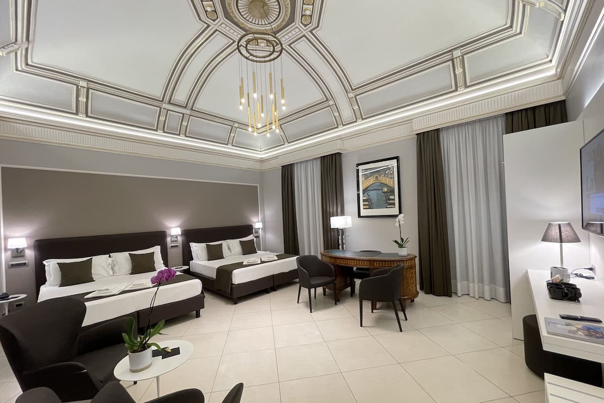 Habitación de hotel con dos camas, un escritorio, una silla, una mesita con una planta y un televisor.