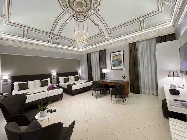 A hotel room with two beds, a desk, a chair, a small table with a plant, and a TV.
