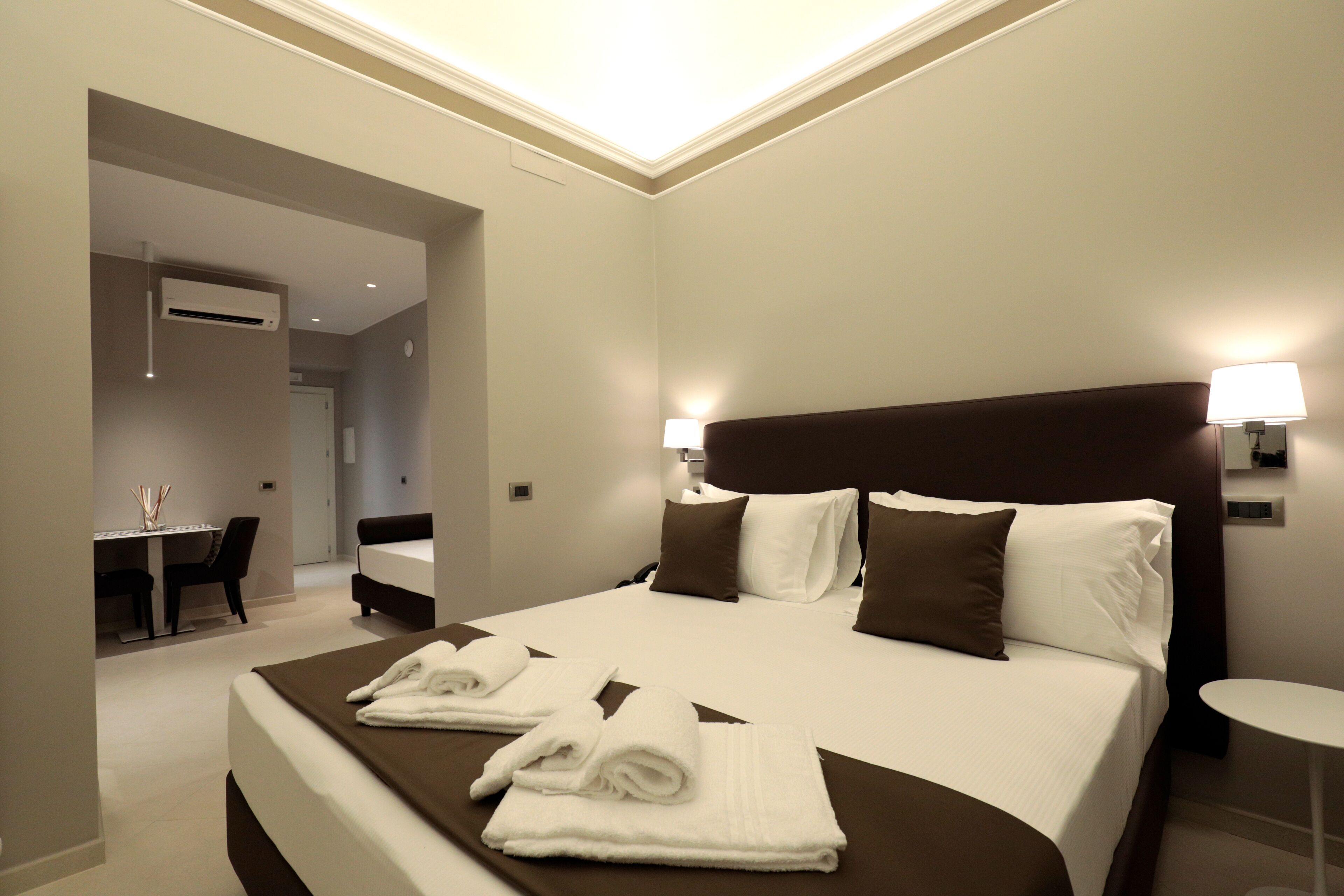 A hotel room with a large bed, two bedside lamps, a small round table, and a desk with chairs.