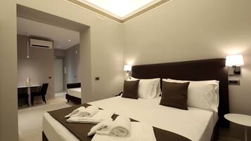 A hotel room with a large bed, two bedside lamps, a small round table, and a desk with chairs.