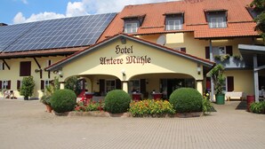 Een hotel met een gele gevel, zonnepanelen op het dak, en een bord met de tekst 'Hotel Alte Mühle'.