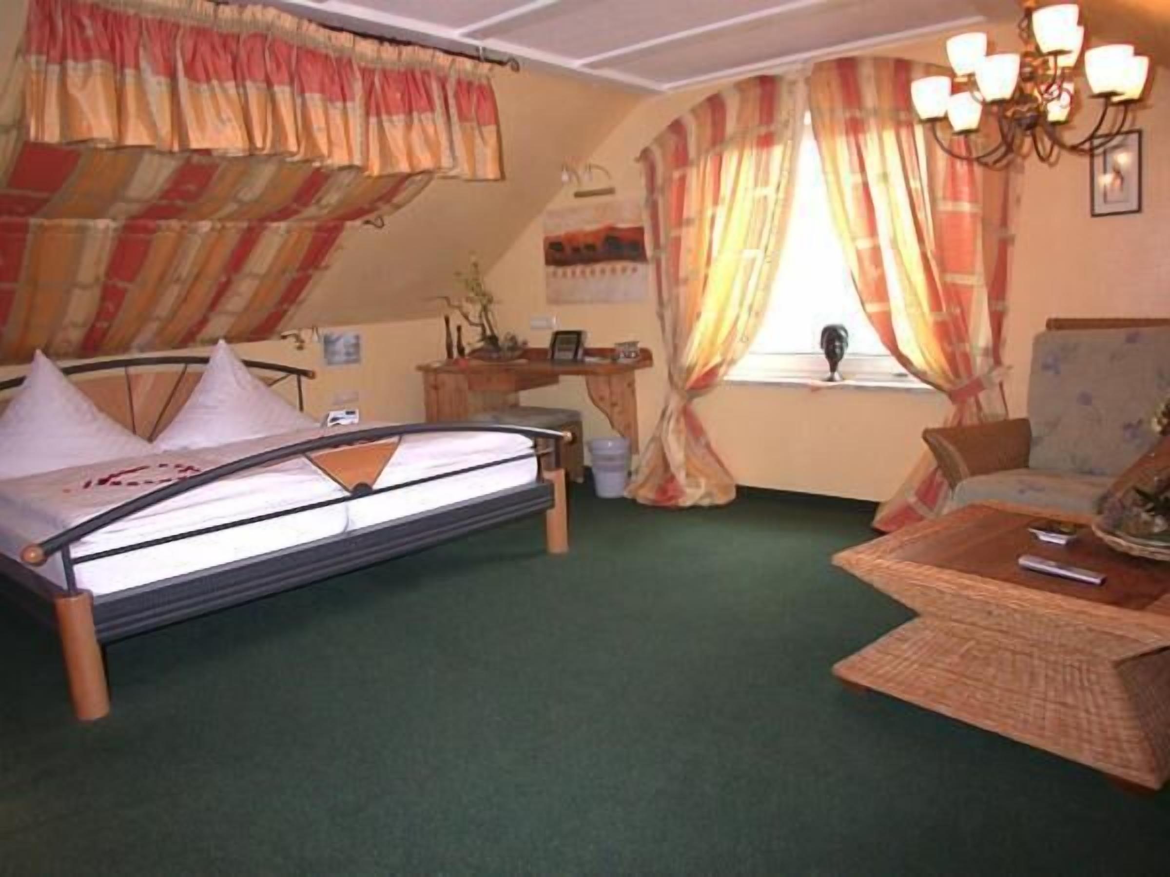 Une pièce comprenant un lit, un bureau, une chaise et une fenêtre avec des rideaux.