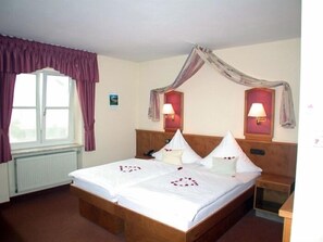 A hotel room with a large bed, two bedside lamps, a window with curtains, and a radiator. - Untere Mühle 1 (Langerringen)