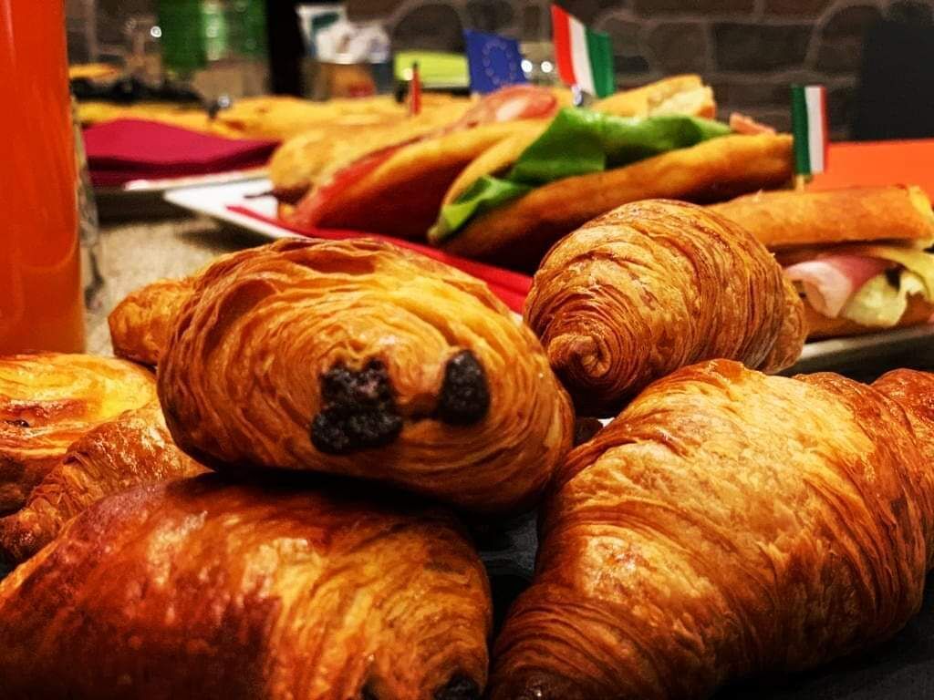 A variety of pastries, including croissants and sandwiches, displayed in a bakery setting.