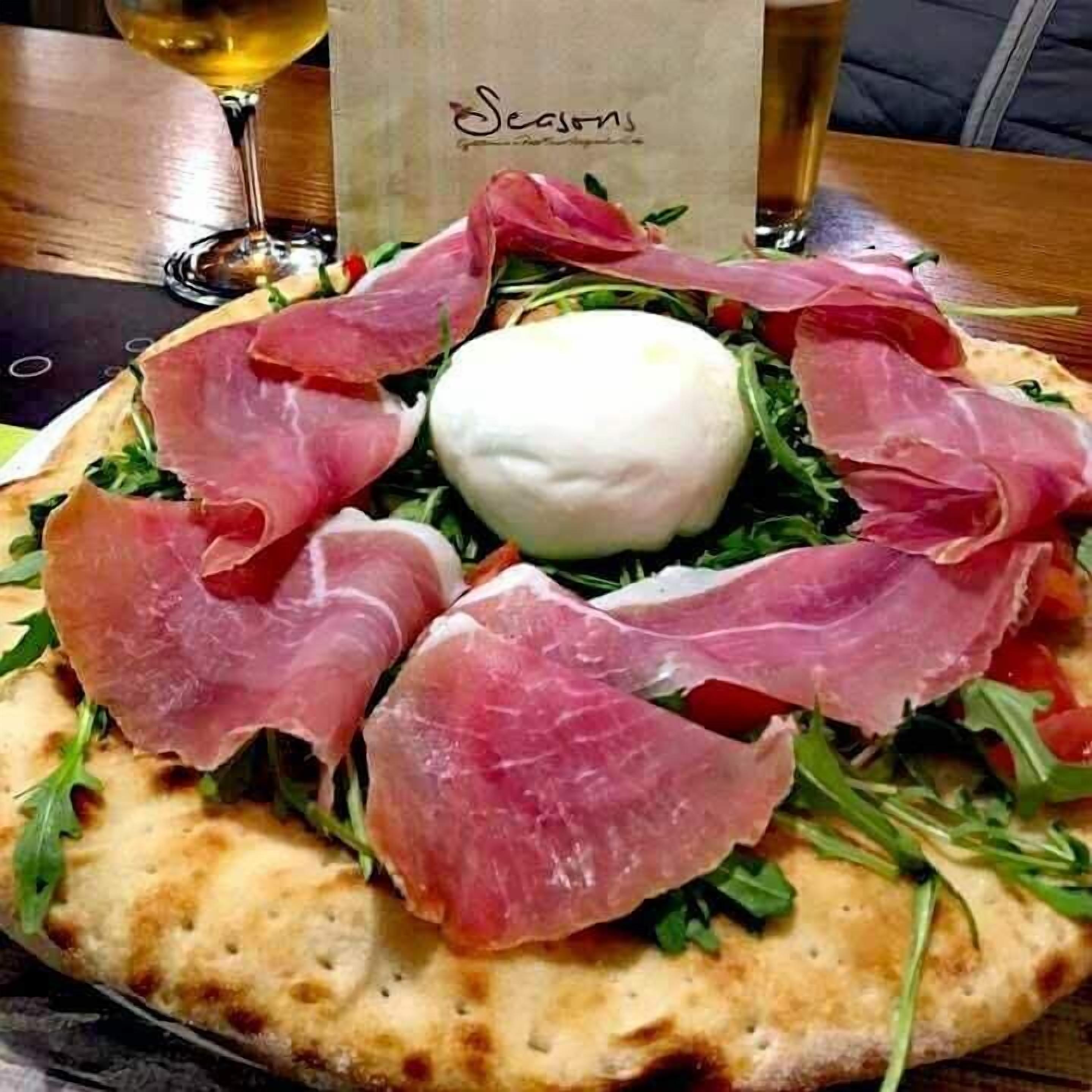 A pizza with prosciutto and arugula on a wooden table.
