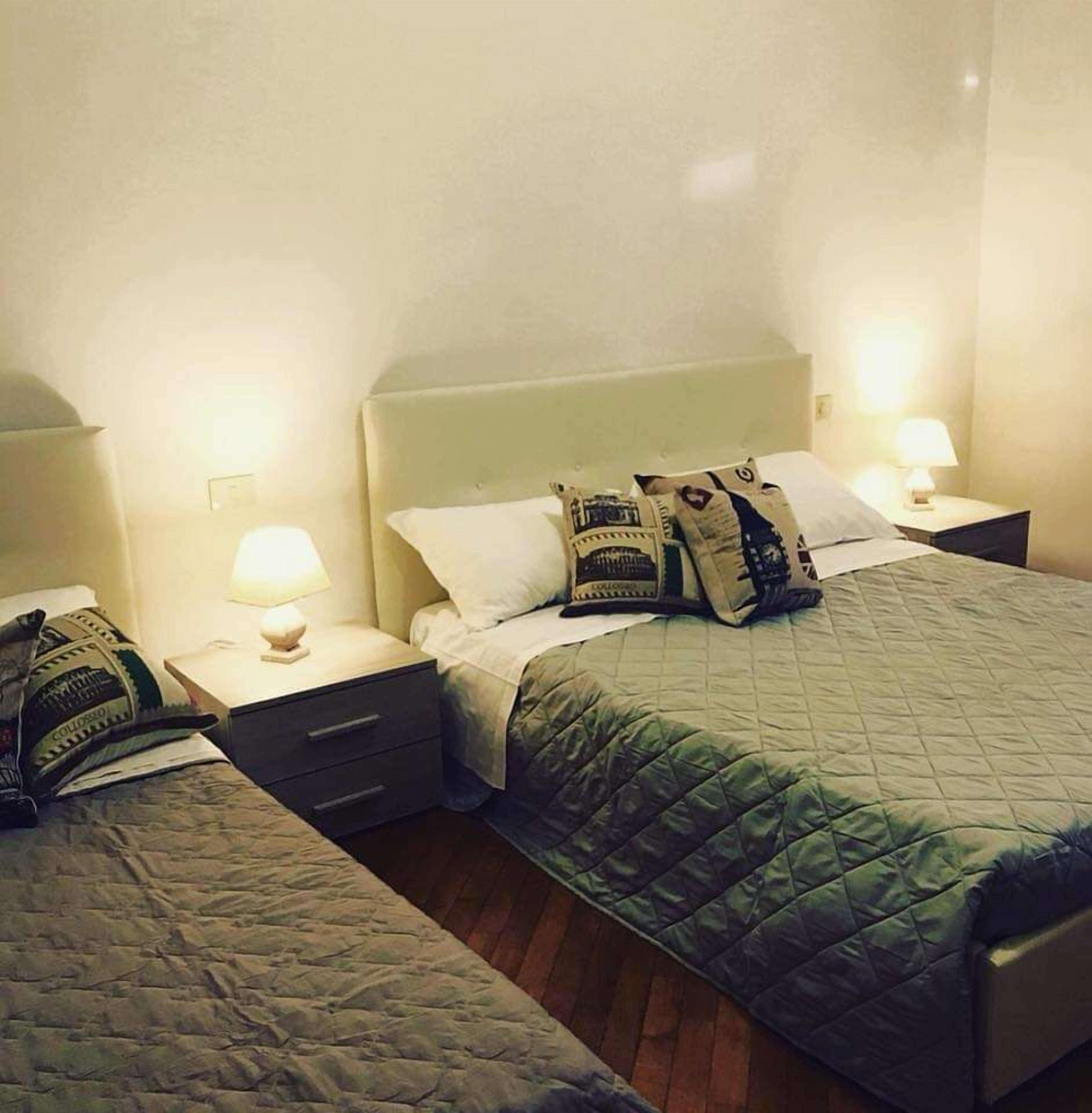 Une chambre d’hôtel avec un grand lit, deux tables de chevet et une petite table de nuit avec une lampe.
