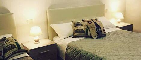 Una habitación de hotel con una cama grande, dos mesitas de noche y una mesilla con lámpara.