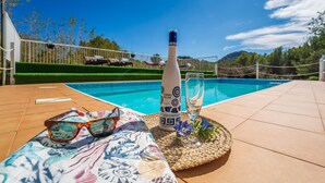 A poolside area with a bottle of alcohol, a glass, and sunglasses on a patterned cloth.