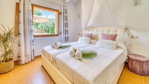 A bedroom with a bed, a window, curtains, a potted plant, and a bedside table.