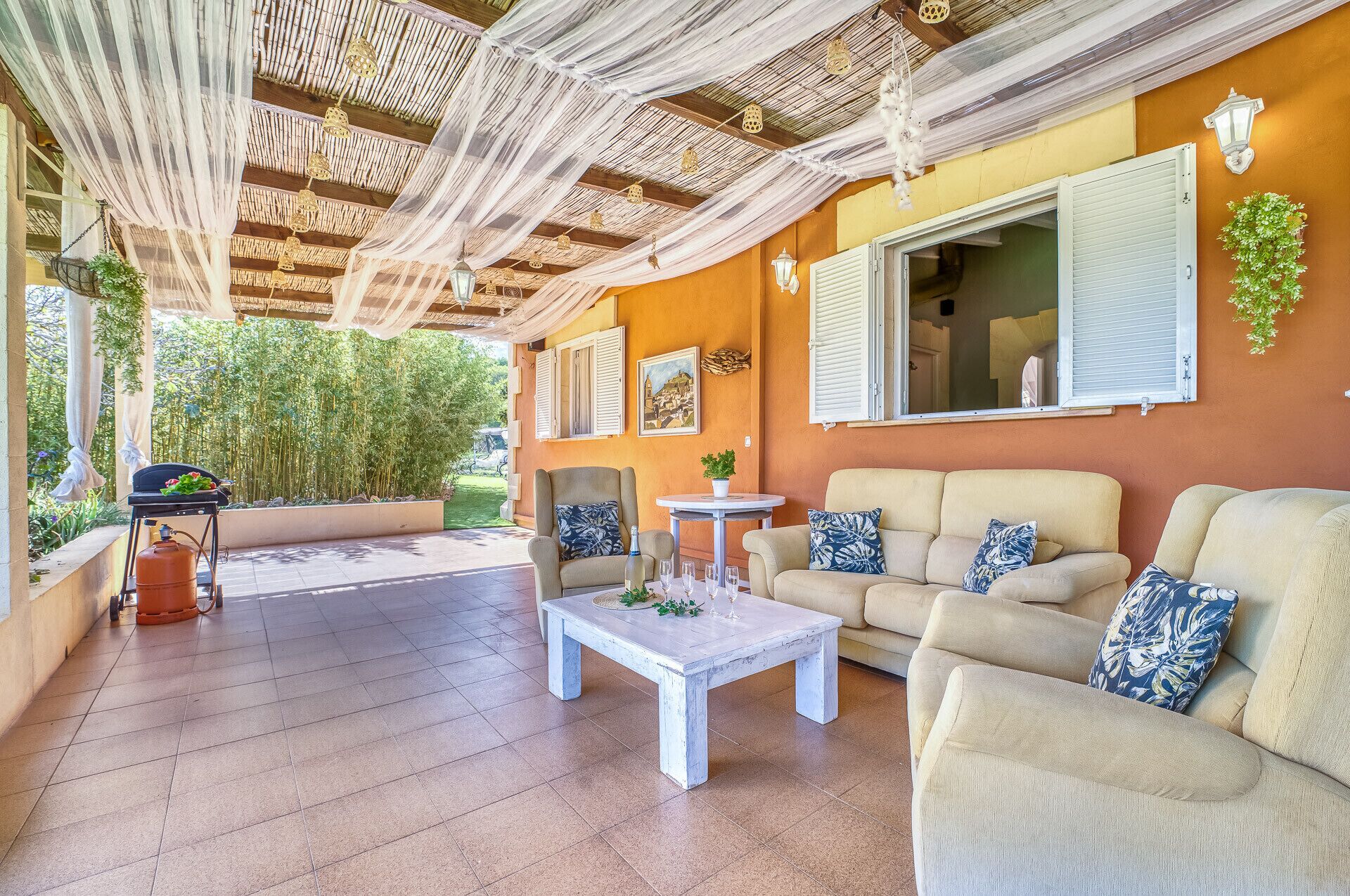 A covered outdoor seating area with a wooden ceiling, beige sofas, and a white coffee table.