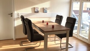 A dining area with a wooden table and black chairs, a ceiling fan, and a clock on the wall. - Cozy and bright furnished apartment centrally located (Norderney)