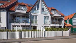 A row of modern, two-story houses with red-tiled roofs, white exteriors, and balconies. - Cozy and bright furnished apartment centrally located (Norderney)