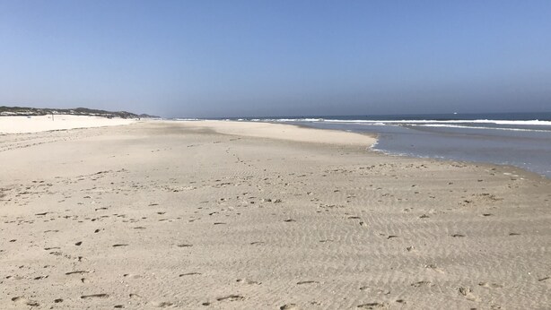 A wide sandy beach with footprints leading to the water, a clear sky, and distant hills. - Cozy and bright furnished apartment centrally located (Norderney)
