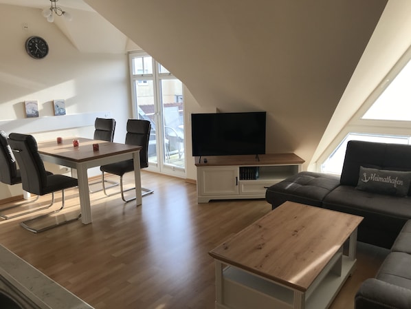 A modern living space with a dining area, a TV, and a sofa.
