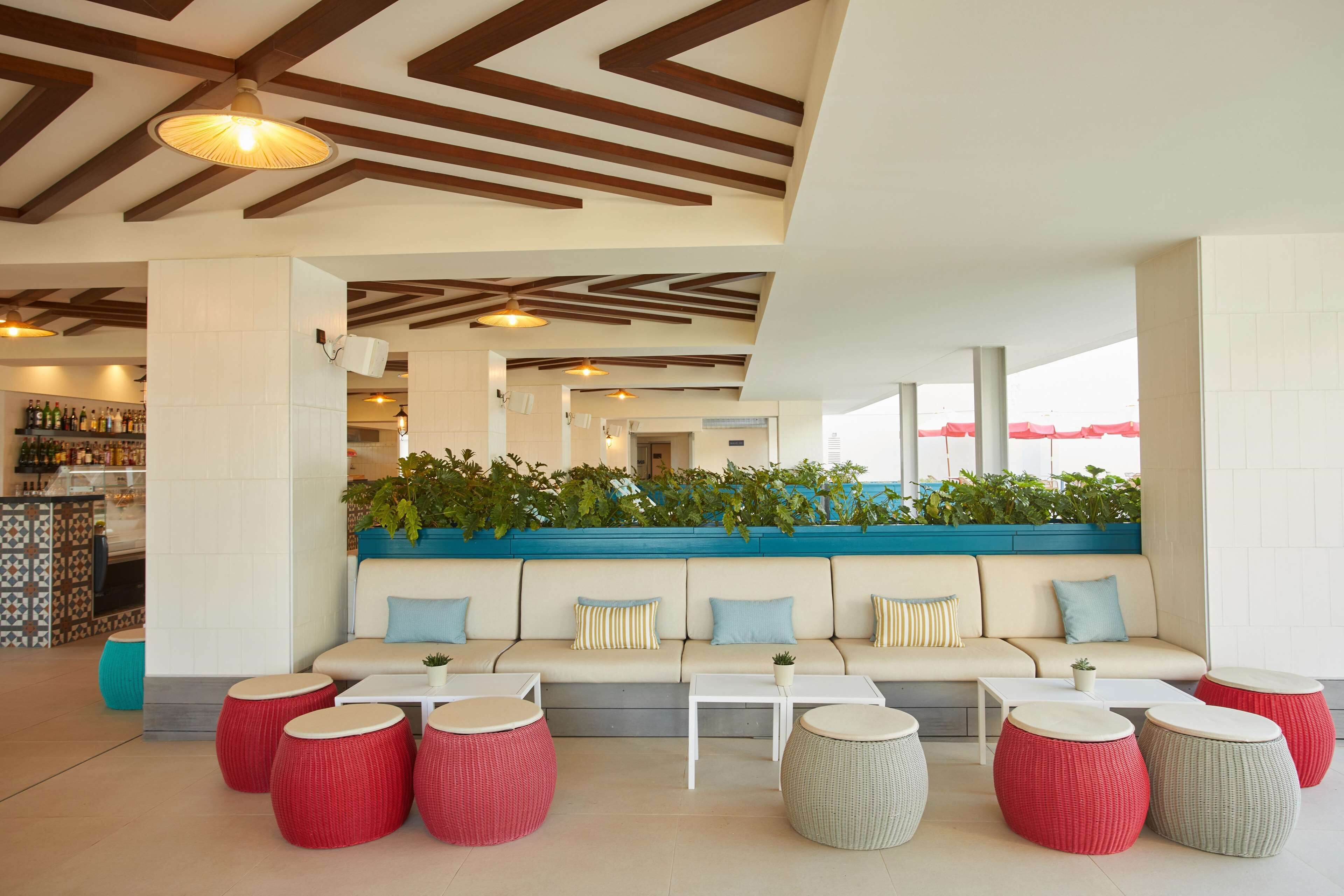 A modern lounge area with a sofa, round tables, and potted plants.