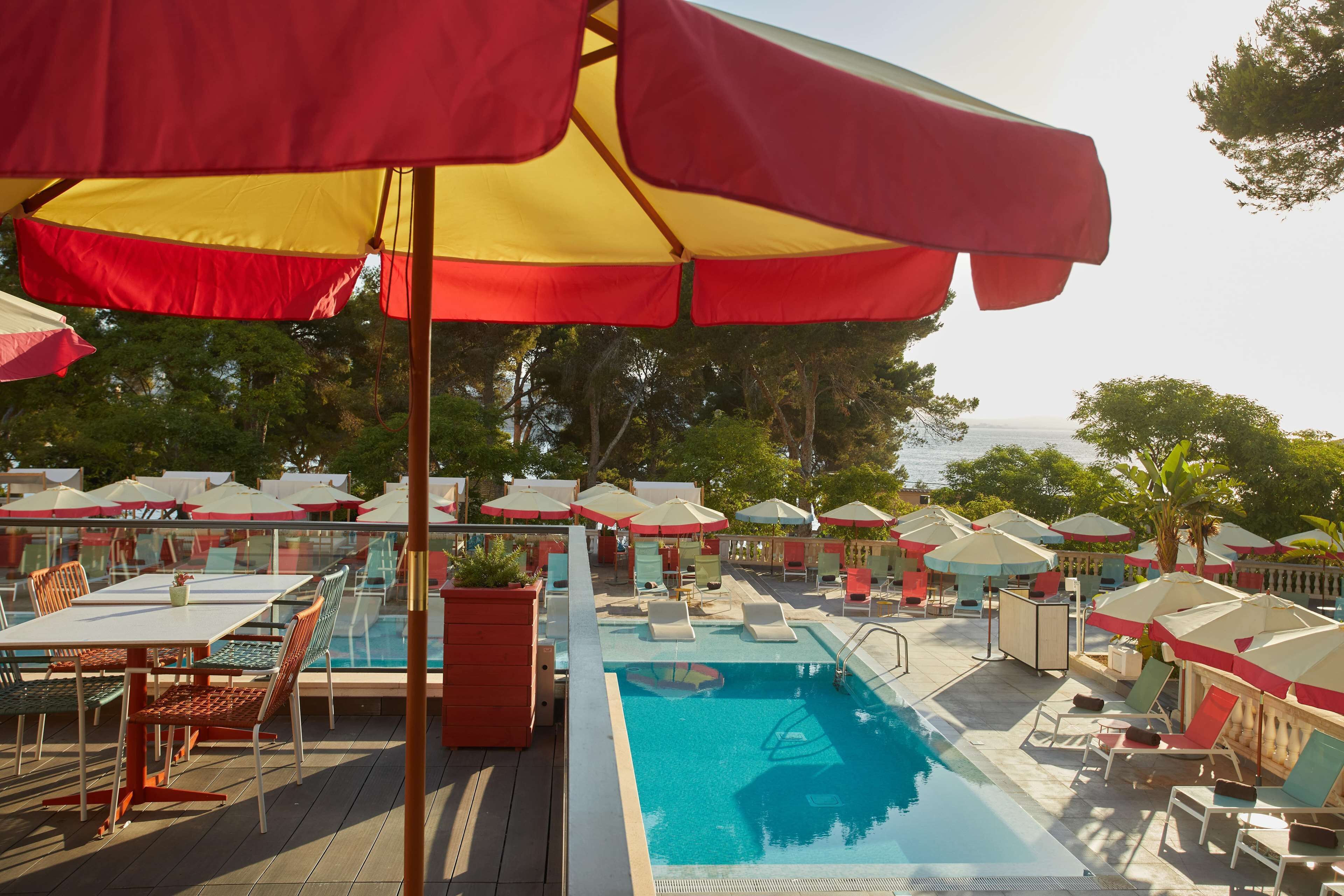 A poolside area with lounge chairs and umbrellas, a pool, and a view of the sea.
