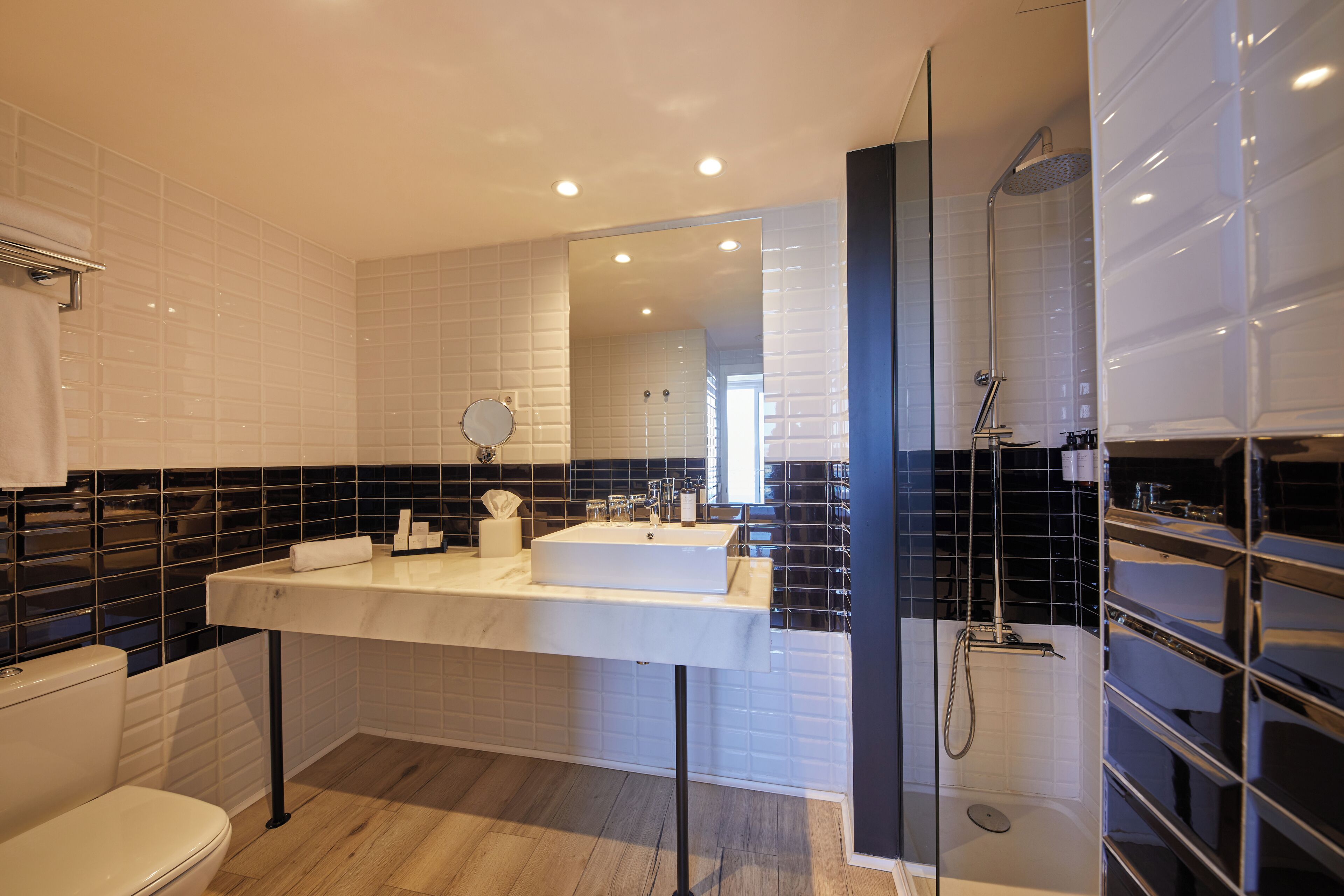 Een moderne badkamer met een wit wastafelmeubel, zwart betegelde wanden en een douchecabine met glazen wanden.