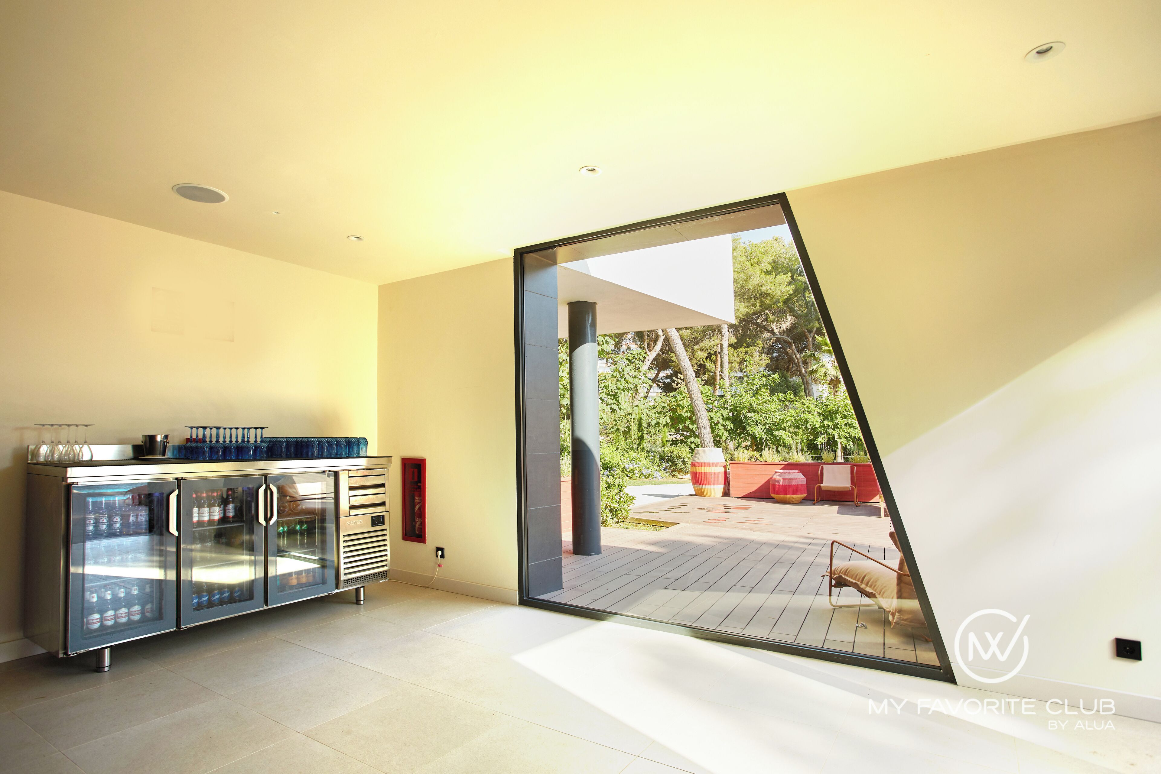 Una cocina moderna con un refrigerador de puerta de vidrio, una encimera de acero inoxidable y una puerta corredera de vidrio que da a un patio exterior.