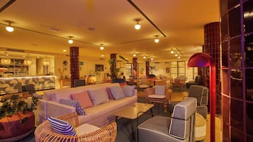 A modern lounge area with a sofa set, wicker chairs, and a bar in the background.