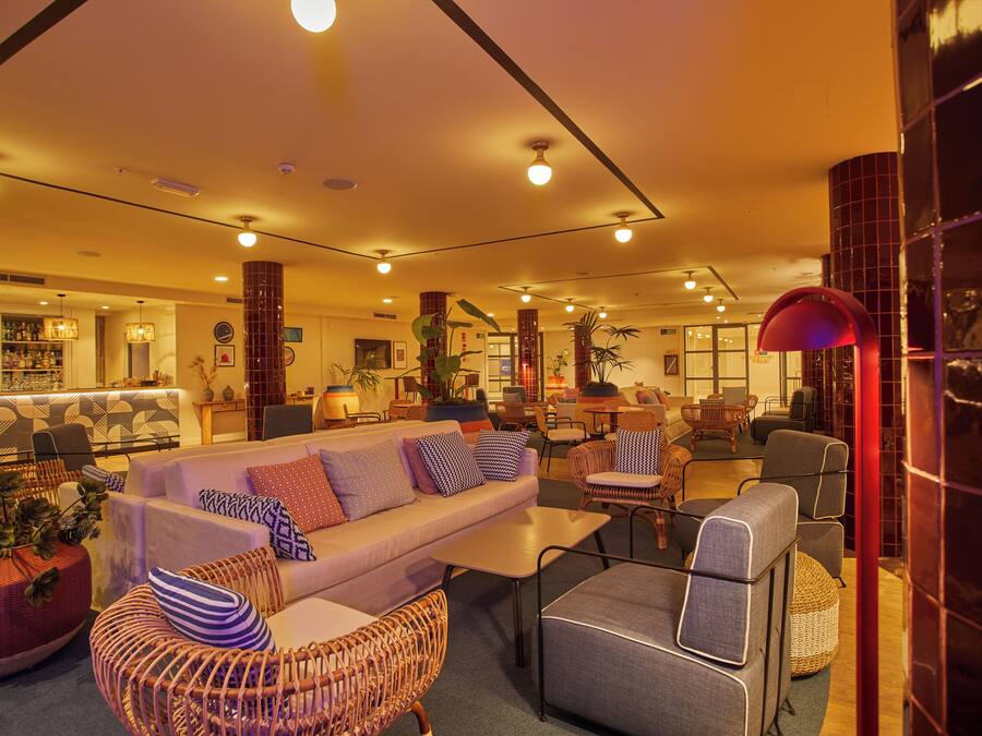A modern lounge area with a sofa set, wicker chairs, and a bar in the background.