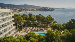 Un hotel con piscina rodeado de árboles, con vistas a una playa y al mar.
