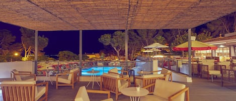 Ein Sitzbereich im Freien mit Holzmöbeln und einem Pool im Hintergrund.
