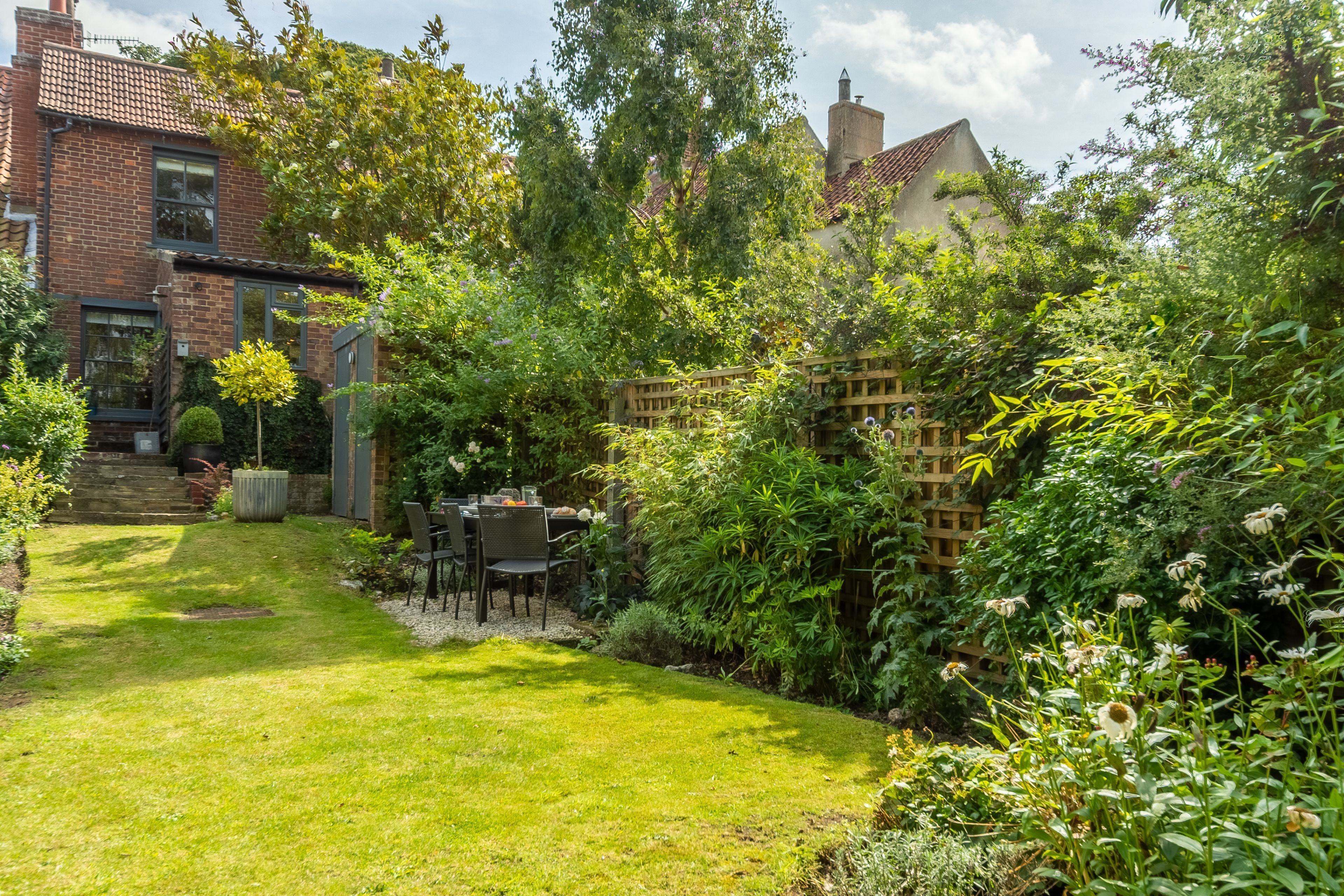 Un jardin bien entretenu, agrémenté d’une terrasse, une maison en briques et une clôture en bois.