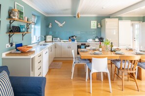A modern kitchen with white cabinets, a wooden dining table, and a blue wall. - Fridays Barn (2), Salthouse, Norfolk (Salthouse)