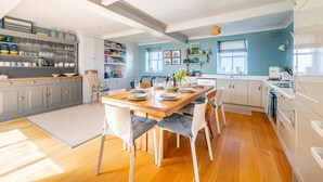 Una cocina moderna con suelo de madera, armarios blancos y un comedor con mesa y sillas de madera.