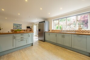 A modern kitchen with light grey cabinets, a stainless steel refrigerator, and a large window with a view of a garden. - Hideaway House, Wells-next-the-Sea, Norfolk (Wells-next-the-Sea)