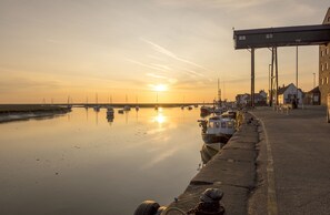 A waterfront scene with boats docked, a pier, and buildings along the shore. - Hideaway House, Wells-next-the-Sea, Norfolk (Wells-next-the-Sea)