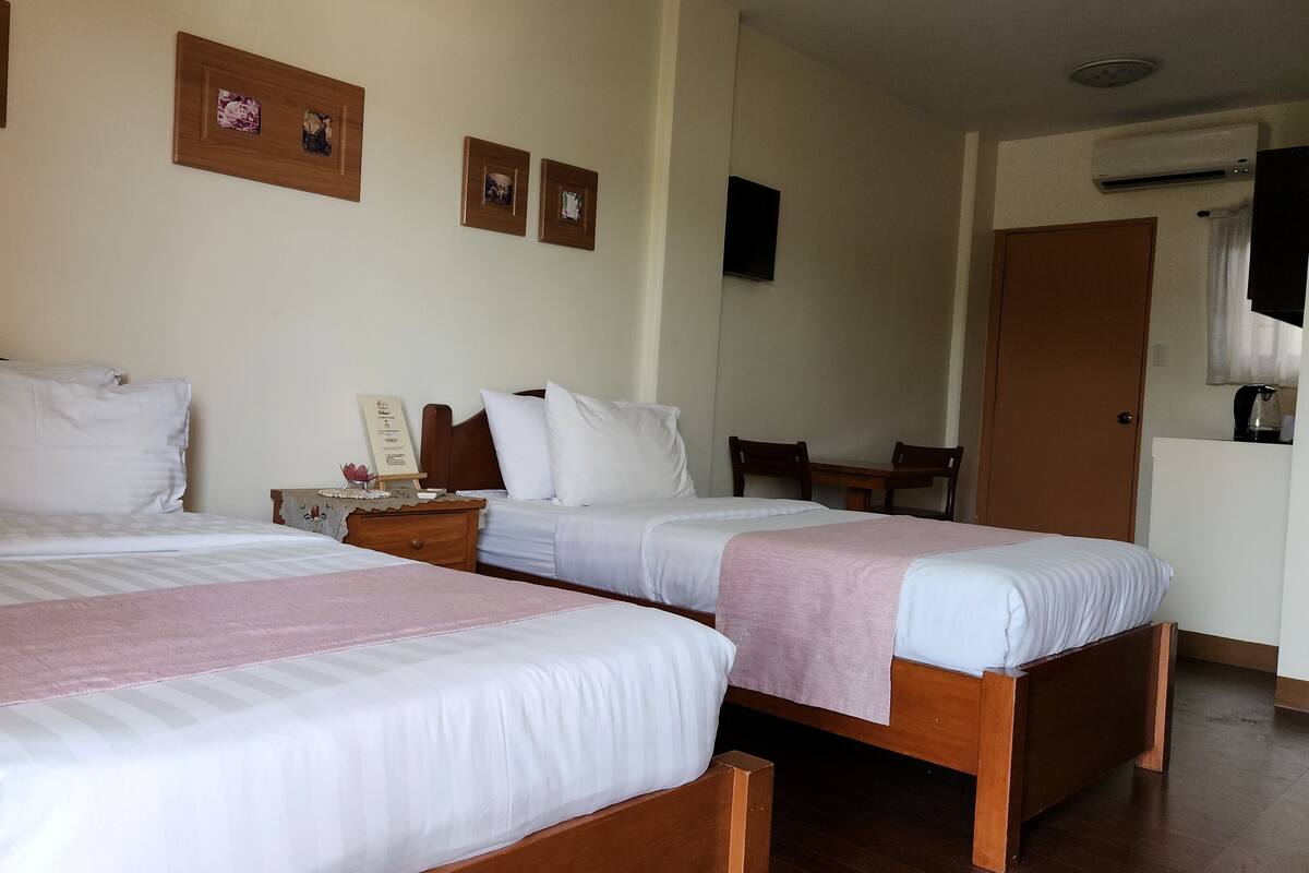 Ein Hotelzimmer mit zwei Betten, einem Nachttisch aus Holz, einem kleinen Tisch mit Stühlen und einem an der Wand hängenden Kunstwerk.